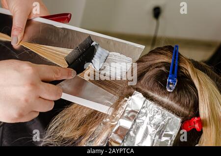 Procedimento di applicazione della polvere decolorante sui capelli dei clienti e di avvolgimento nella lamina. Tecnica Airtouch Foto Stock