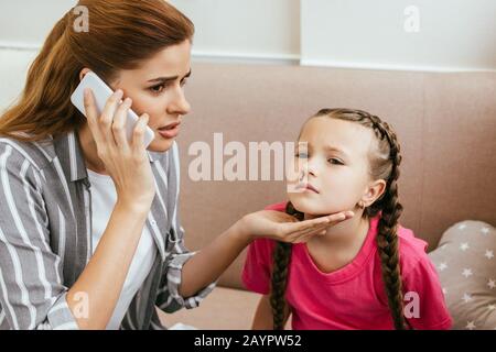 la madre preoccupata che ha consultato online lo smartphone mentre sua figlia ha avuto sanguinamento nasale Foto Stock