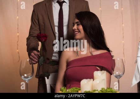 vista ritagliata di un uomo elegante che presenta rosa rossa alla ragazza felice sui valentines Foto Stock