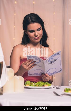 attraente, elegante menu lettura ragazza mentre si siede nel ristorante Foto Stock