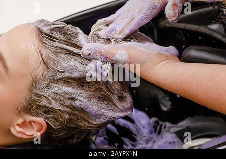 Stylist per capelli applicazione di shampoo colorito viola dopo la tintura dei capelli. Primo piano. Foto Stock