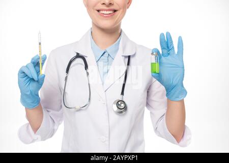 Vista ritagliata di una siringa sorridente che tiene il medico e di un vaccino verde isolato su bianco Foto Stock