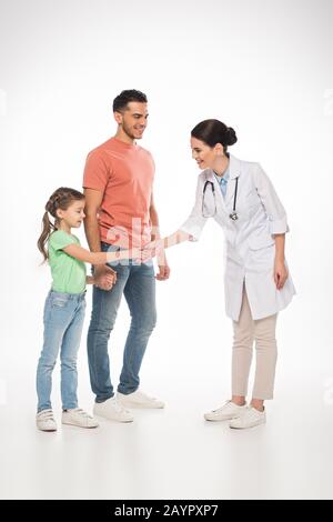 Tutta la lunghezza delle mani sorridenti di agitazione del pediatra con il capretto vicino al padre sullo sfondo bianco Foto Stock