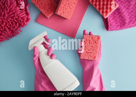 vista dal taglio corto della governante in guanti di gomma rosa con spugna e flacone spray su blu con stracci Foto Stock