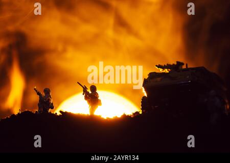 Silhouette di guerrieri giocattolo e canotta sul campo di battaglia con tramonto e fuoco sullo sfondo Foto Stock