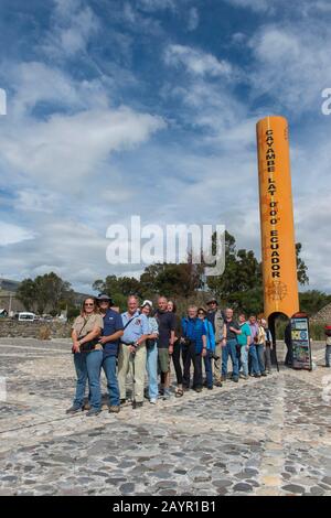 Un gruppo di tour è in piedi con un piede nell'emisfero settentrionale e l'altro piede nell'emisfero meridionale presso il monumento equatore Quitsato e s. Foto Stock