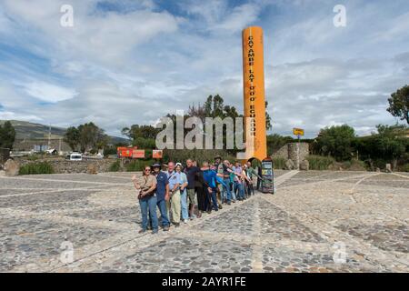 Un gruppo di tour è in piedi con un piede nell'emisfero settentrionale e l'altro piede nell'emisfero meridionale presso il monumento equatore Quitsato e s. Foto Stock