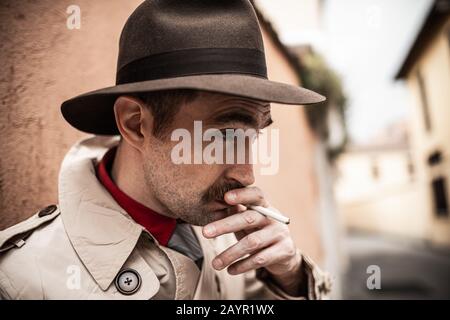 Spia detective che cammina in una città mentre fuma una sigaretta Foto Stock