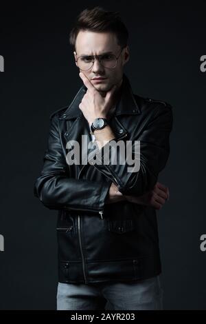 un uomo dal design elegante e carico di tensione con giacca biker isolata su nero Foto Stock