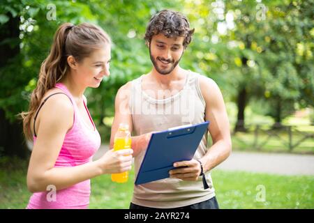 Uomo sorridente che mostra un tavolo da allenamento a una donna, formazione personale e concetto di fitness Foto Stock