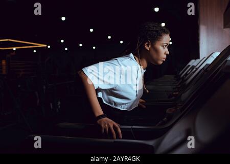 Vista laterale della donna afroamericana che corre sul tapis roulant in palestra Foto Stock