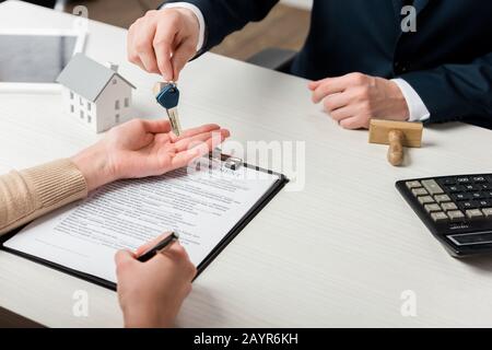 vista ritagliata del realtor che dà la chiave alla donna che firma il contratto, concetto di leasing Foto Stock