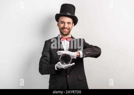 felice mago professionista che tiene palla magica, sul grigio Foto Stock