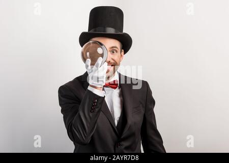 mago professionista che tiene palla magica, isolato su grigio Foto Stock