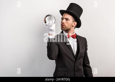 mago professionista interessato che tiene palla magica, isolato su grigio Foto Stock