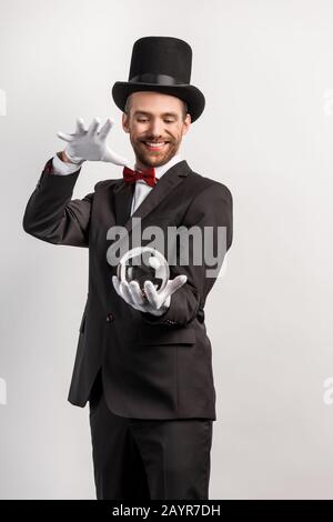 felice mago professionista che tiene palla magica, isolato su grigio Foto Stock