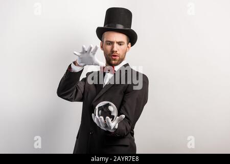 mago professionista focalizzato che tiene palla magica, isolato su grigio Foto Stock