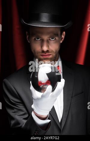 mago professionista che tiene palla magica in circo con tende rosse Foto Stock