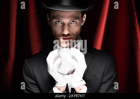 mago professionista che tiene palla magica in circo con tende rosse Foto Stock