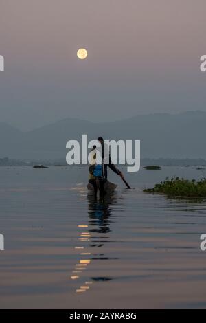 Prima dell'alba sotto una luna piena un pescatore di canottaggio della gamba nella sua barca sta tirando nella sua rete di pesca ha regolato il giorno prima sul lago di Inle in Myanmar. Foto Stock