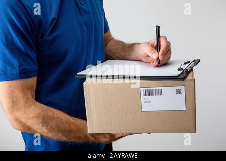 Vista ritagliata della scrittura del corriere sugli appunti e tenendo la scatola di cartone isolata sul grigio Foto Stock