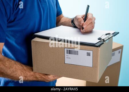 Vista ritagliata della scrittura del corriere sulla clipboard su scatola di cartone con pacchetti isolati su blu Foto Stock