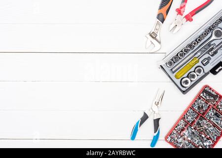 Vista dall'alto delle cassette portautensili con chiavi, bulloni e pinze per dadi su superficie in legno bianca Foto Stock