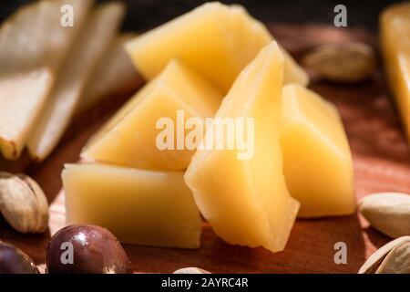 Selezione di pezzi di grana padano con olive, fettine di pera e pistacchi su sfondo ligneo Foto Stock