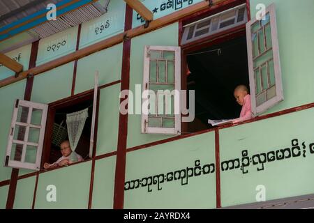 Giovani suore che guardano fuori dalla loro finestra dormitorio a Zayertheingi, un nunnery buddista a Sagaing, una città fuori Mandalay, Myanmar. Foto Stock
