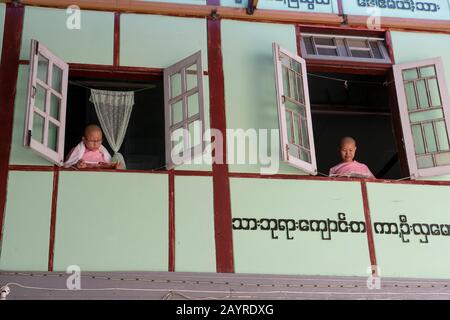 Giovani suore che guardano fuori dalla loro finestra dormitorio a Zayertheingi, un nunnery buddista a Sagaing, una città fuori Mandalay, Myanmar. Foto Stock