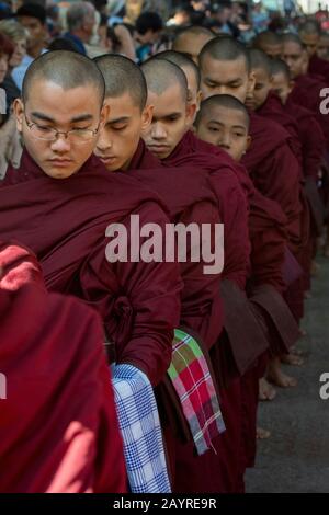 I monaci buddisti, circondati da centinaia di turisti, si stanno schierando per ricevere le loro elemosine (pasto) al Monastero di Mahagandayon a Mandalay, Myanmar. Foto Stock