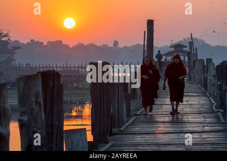 Monaci buddisti che camminano all'alba sul ponte U Bein (costruito intorno al 1850 e si ritiene che sia il più antico e più lungo ponte di legno di teak del mondo) spann Foto Stock