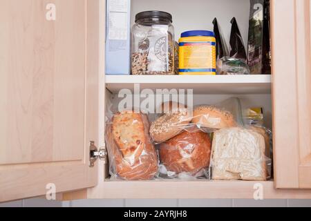 Varietà di pane conservato in sacchetti di plastica in armadio in cucina Foto Stock