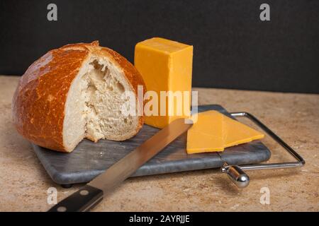 Pane con pane e pane con pane scomposto e cheddar e fette su un affettatrice, con un coltello per il pane Foto Stock