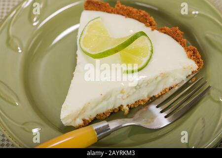 Fetta di torta di calce chiave, con una fetta di calce intrecciata in alto, appoggiata su un piatto cinese su una tovaglia con un motivo floreale Foto Stock