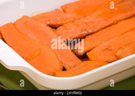 Patate dolci candite al forno in una teglia rettangolare su un piano rustico in legno sullo sfondo Foto Stock