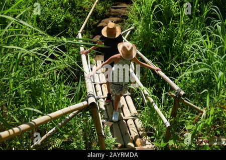 Due giovani adolescenti che attraversano un ponte di bambù sulle risaie di Bali Foto Stock