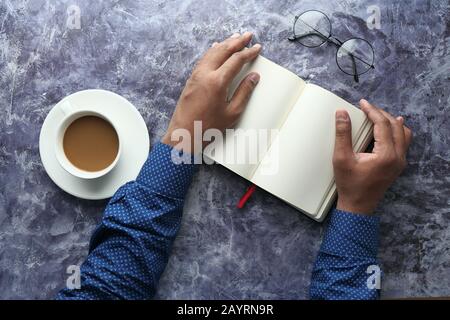 vista dall'alto della mano dell'uomo sul diario e del tè sul tavolo Foto Stock