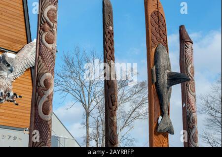 Pali in legno intagliato Ainu di fronte al centro di spettacolo Ainu in Ainu Kotan, che è un piccolo villaggio Ainu in Akankohan nel Parco Nazionale di Akan, Hokk Foto Stock