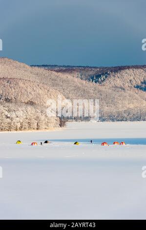 Vista del lago ghiacciato Abashiriko e della foresta coperta di neve vicino Abashiri, una città sull'Isola di Hokkaido, Giappone, con tende colorate allestite sul ghiaccio per Foto Stock