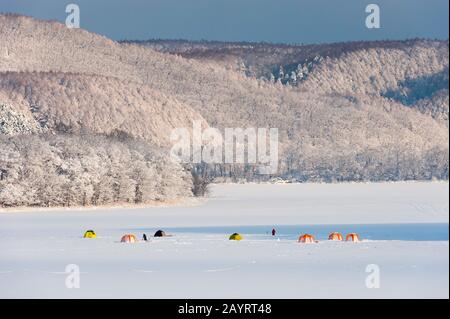 Vista del lago ghiacciato Abashiriko e della foresta coperta di neve vicino Abashiri, una città sull'Isola di Hokkaido, Giappone, con tende colorate allestite sul ghiaccio per Foto Stock