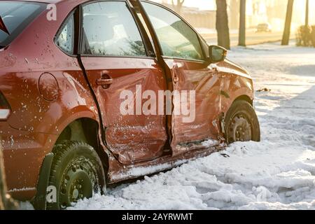 il lato rotto e ammaccato di una vettura rossa. incidente invernale su una strada sdrucciolevole, la vettura volava sul lato della strada. Primo piano, neve Foto Stock