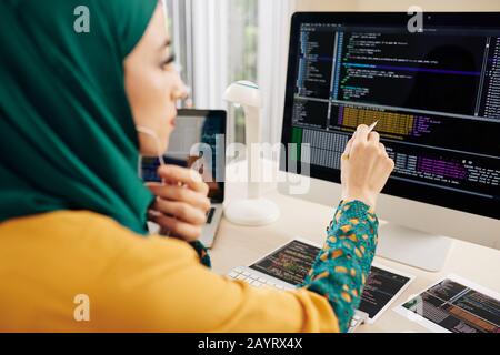 Giovane sviluppatore di software musulmano che controlla le stringhe nel codice di programmazione sullo schermo del computer Foto Stock