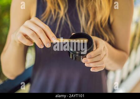 Giovane donna spazzolare i denti usando polvere di carbone Attivo per spazzolare e sbiancare i denti. Spazzola ecologica di bambù Foto Stock