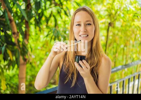 Giovane donna spazzolare i denti usando polvere di carbone Attivo per spazzolare e sbiancare i denti. Spazzola ecologica di bambù Foto Stock