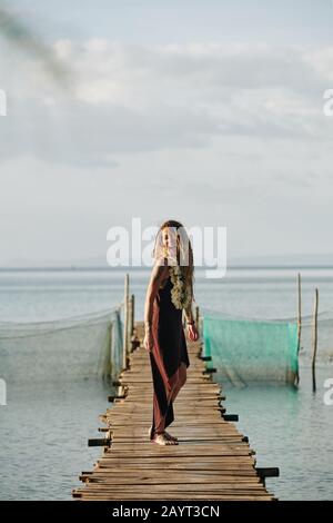 Bella giovane donna felice con lunghe temute in piedi sul molo di legno Foto Stock