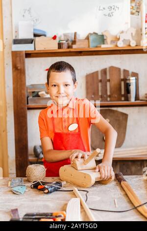 il ragazzo costruisce e gioca con il giocattolo di legno nel laboratorio Foto Stock