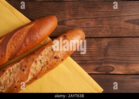 Due baguette croccanti francesi mentono tovaglioli di stoffa gialla tabella di legno baguettes di fondo in assortimento con semi di sesamo dolci classici nazionali francesi Foto Stock