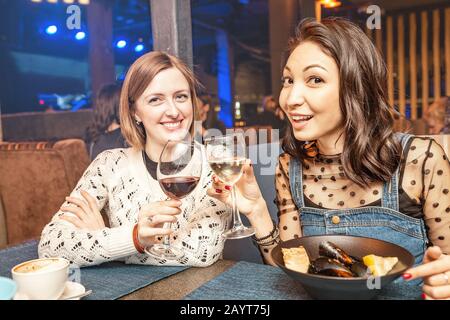 Due amici ragazza hanno divertimento e chiacchierare mentre beve un bicchiere di vino in un ristorante in un night club. Il concetto di relax e di cittadinanza Foto Stock