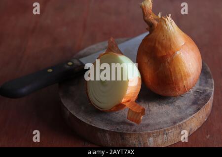 Cipolle su un tagliere di legno in un tono scuro e moody Foto Stock